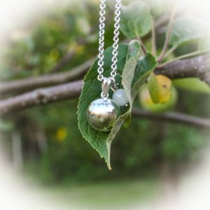 Omenapuunlehdellä hopeinen palloriipus sekä pieni riipus vaaleansiniselä kivihelmellä